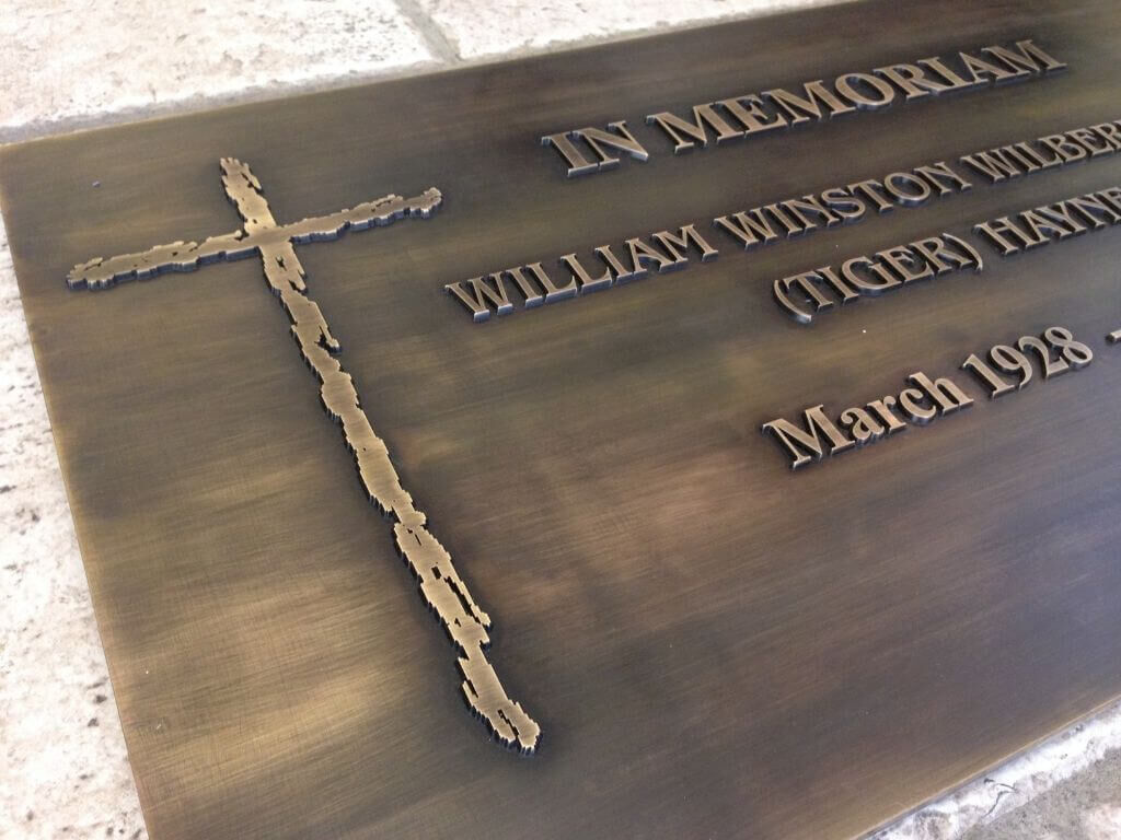 Detailaufnahme des erhabenen Kreuzes und Schrift der Gedenktafel aus patiniertem Messing Detailaufnahme des erhabenen Kreuzes und Schrift der Gedenktafel aus patiniertem Messing